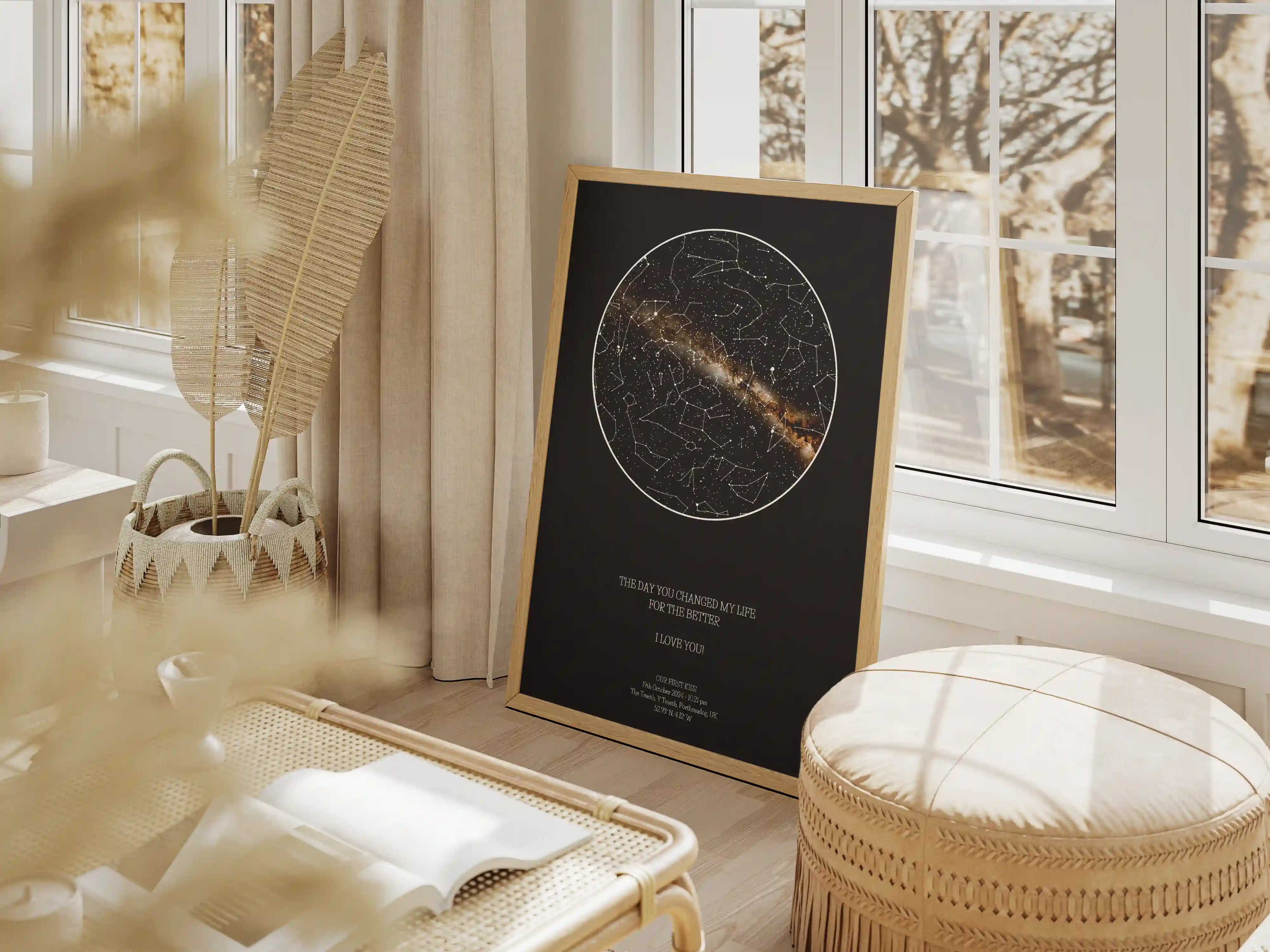 Elegant personalised star map print with a black background and golden milky way with constellations, framed in oak wood, leaning against a sunlit window in a cosy bohemian-inspired living space.