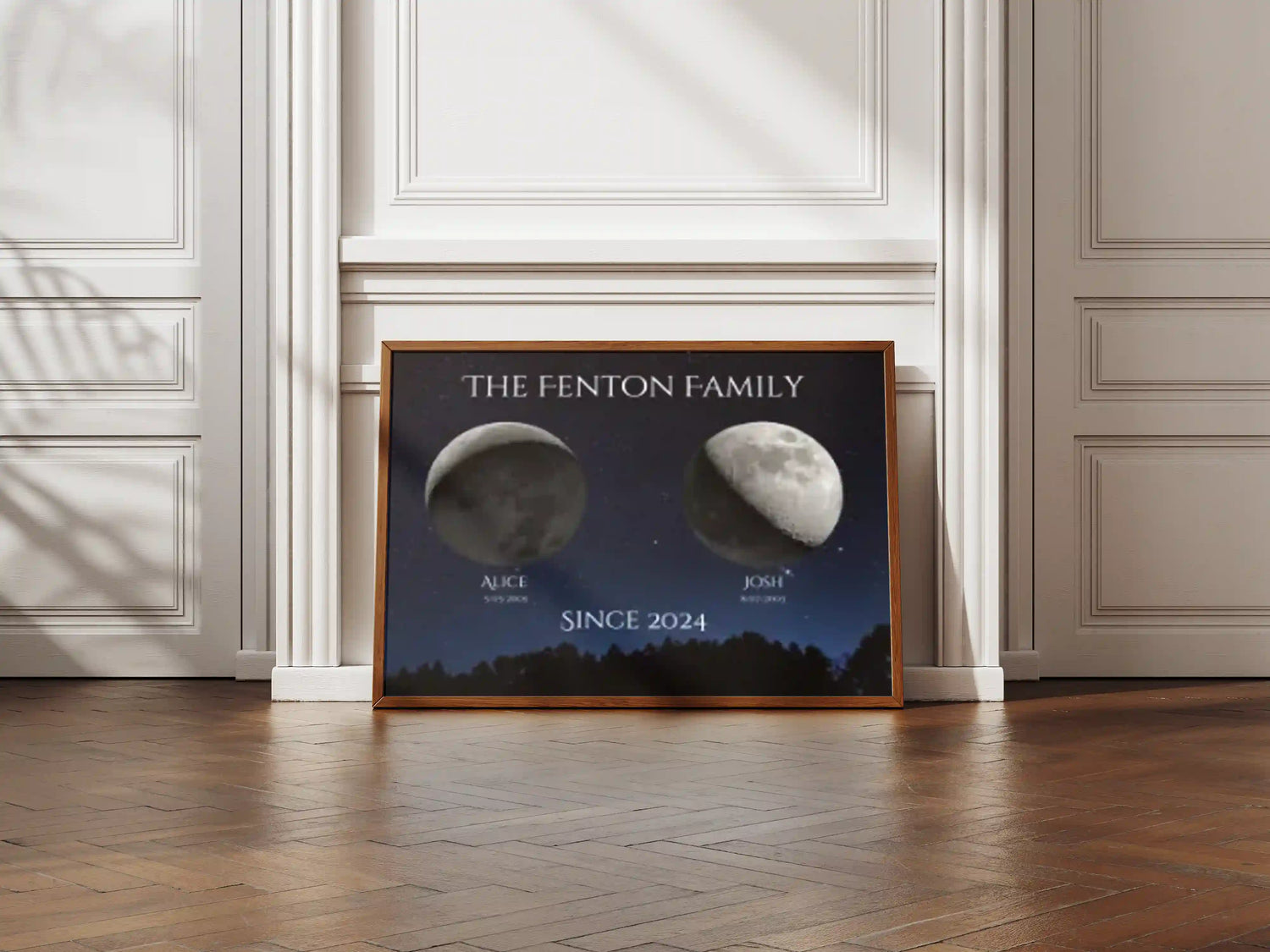 Custom family moon phase print with oak frame, leaning against a white panelled wall in a natural light interior – astronomy-inspired art by Skylit Studio.