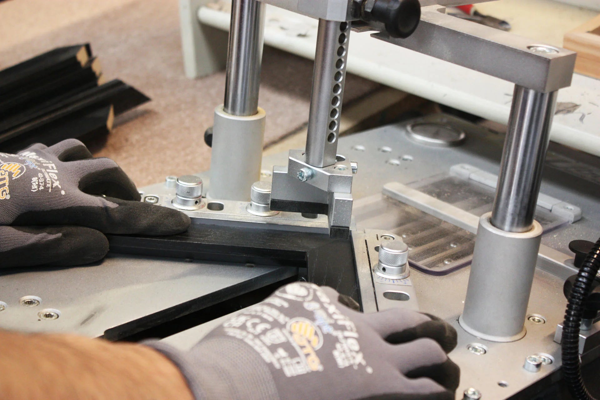 A craftsman wearing protective gloves carefully assembling a black picture frame using a precision framing machine, highlighting the meticulous craftsmanship involved in creating framed star maps.