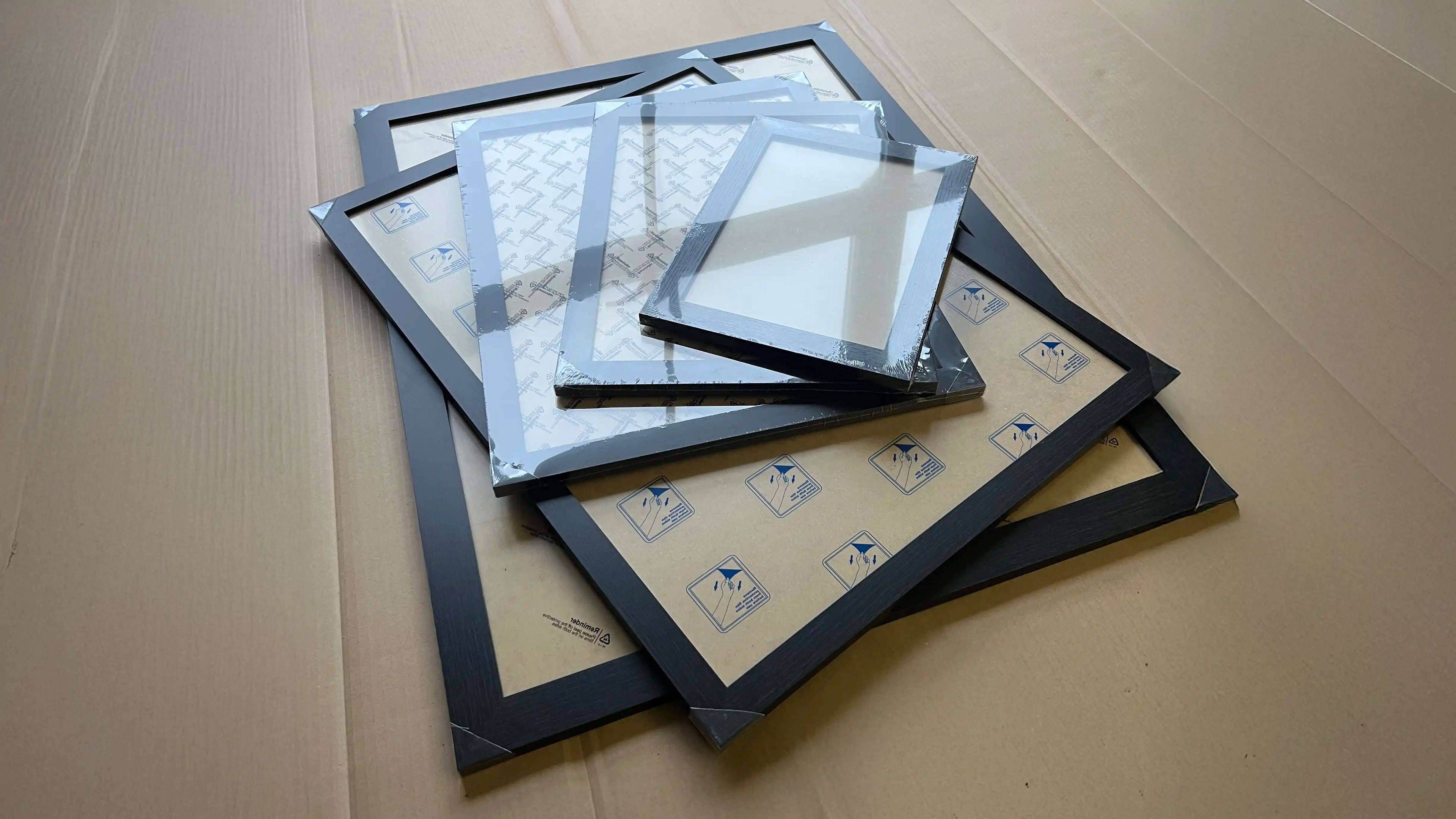 Stack of Skylit Studio’s classic black engineered wood frames in multiple sizes, resting on a large cardboard surface with protective backing and corner covers.