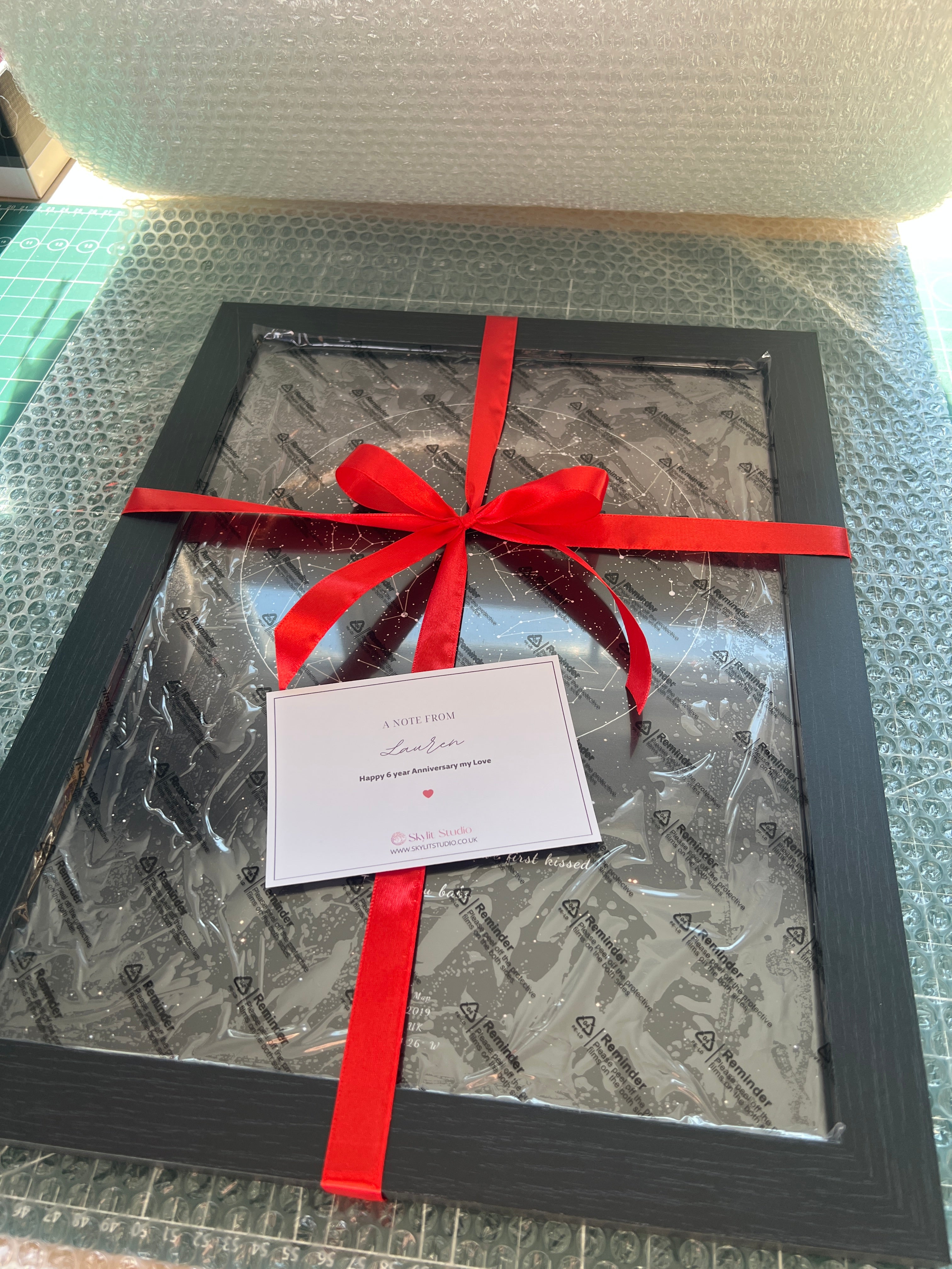 Framed Skylit Studio star map wrapped with a red ribbon and personalised note, presented on protective packaging – ready-to-gift for anniversaries, birthdays, or special moments.