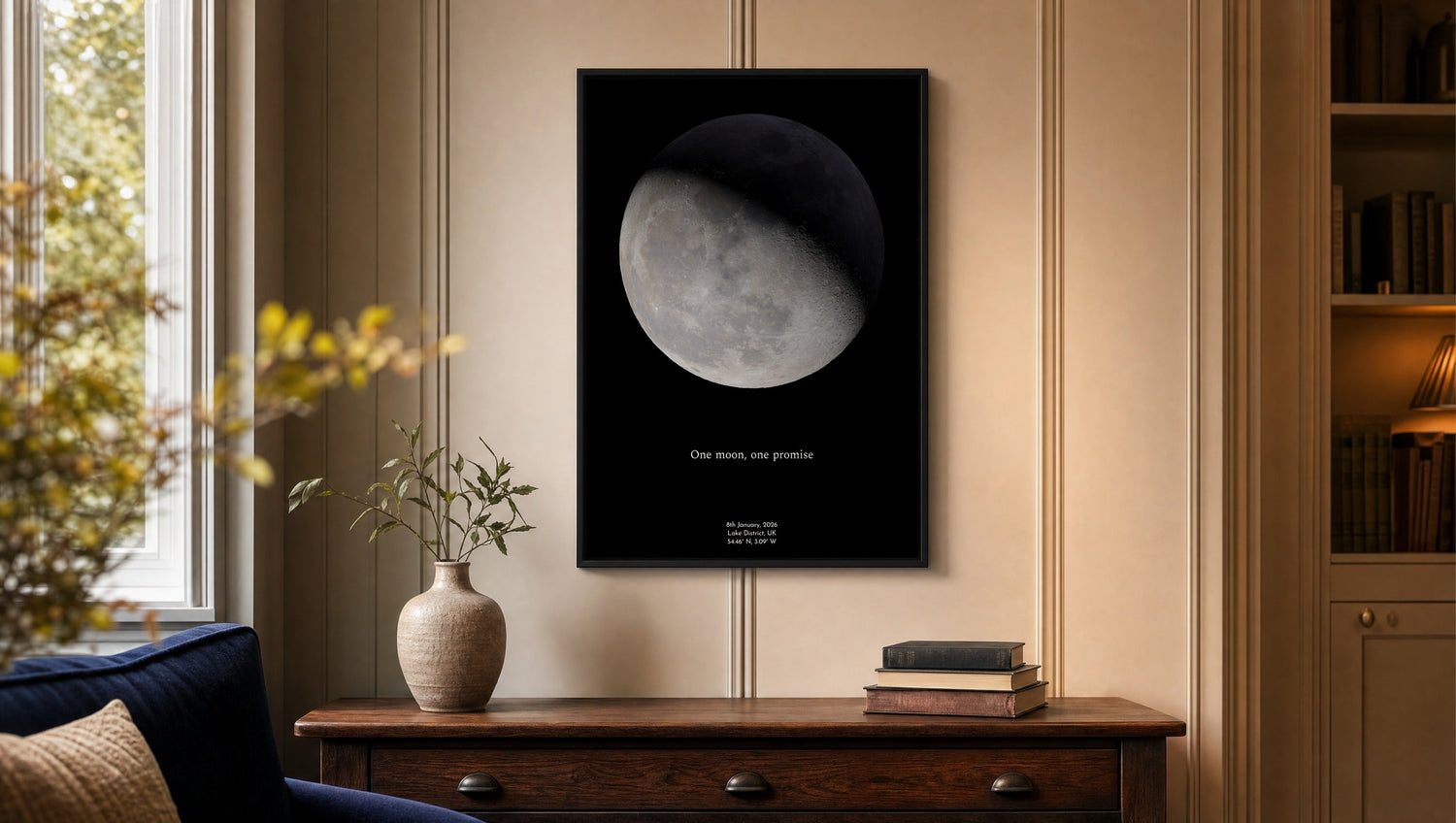 Personalised moon phase print in a black frame on a panelled living-room wall above a wooden console, inscribed ‘One moon, one promise’ with date, Lake District and coordinates, by Skylit Studio