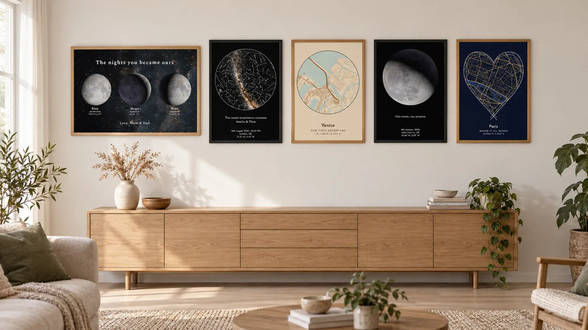 A horizontal run of five framed Skylit prints hung in one line above an oak sideboard: a family moon phases print at the end, then a star map, a Venice map, a moon phase print and a Paris heart map, in alternating oak and black frames