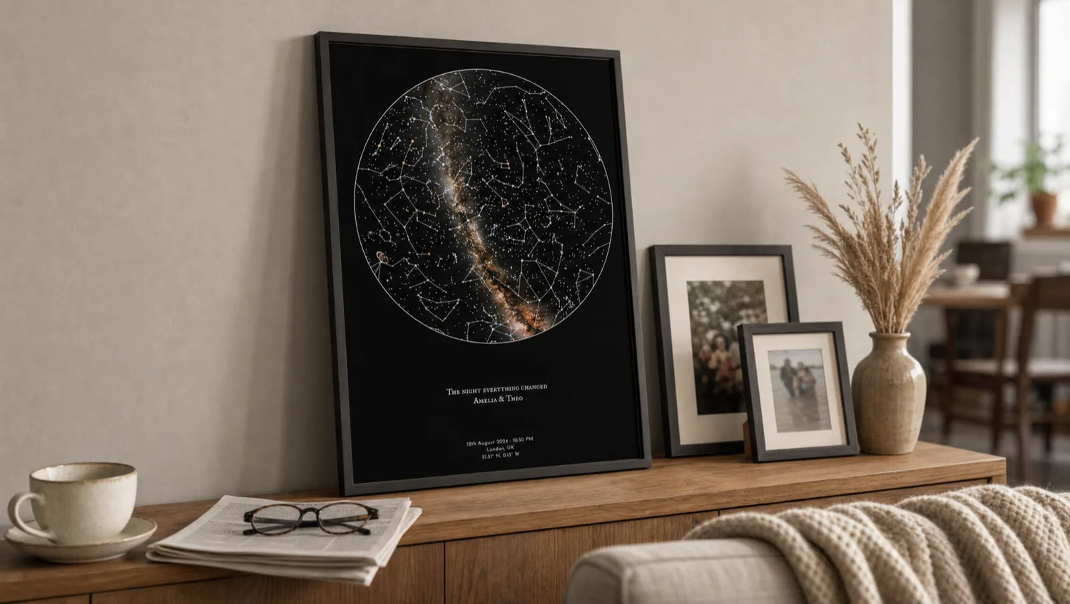 A framed Skylit Studio personalised star map print leaning on a wooden sideboard in a warm living room, styled beside family photo frames, a teacup and dried grasses, a memory-led personalised gift idea for grandparents