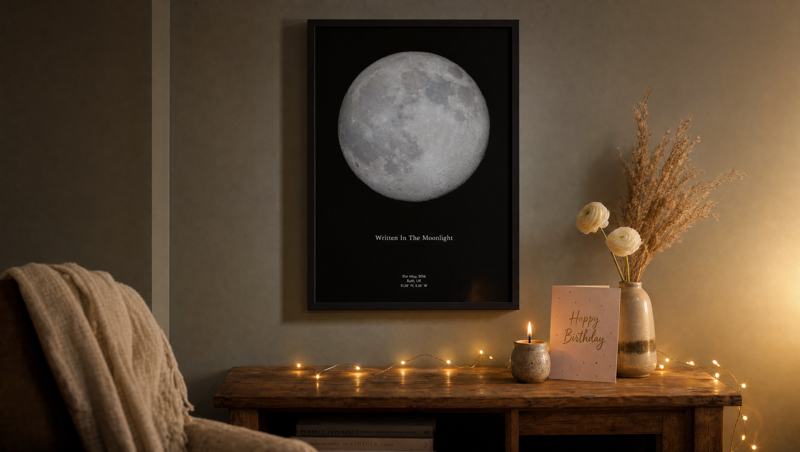 Framed personalised moon phase print hanging above a cosy console table, styled as a birthday gift with a lit candle, birthday card and string lights