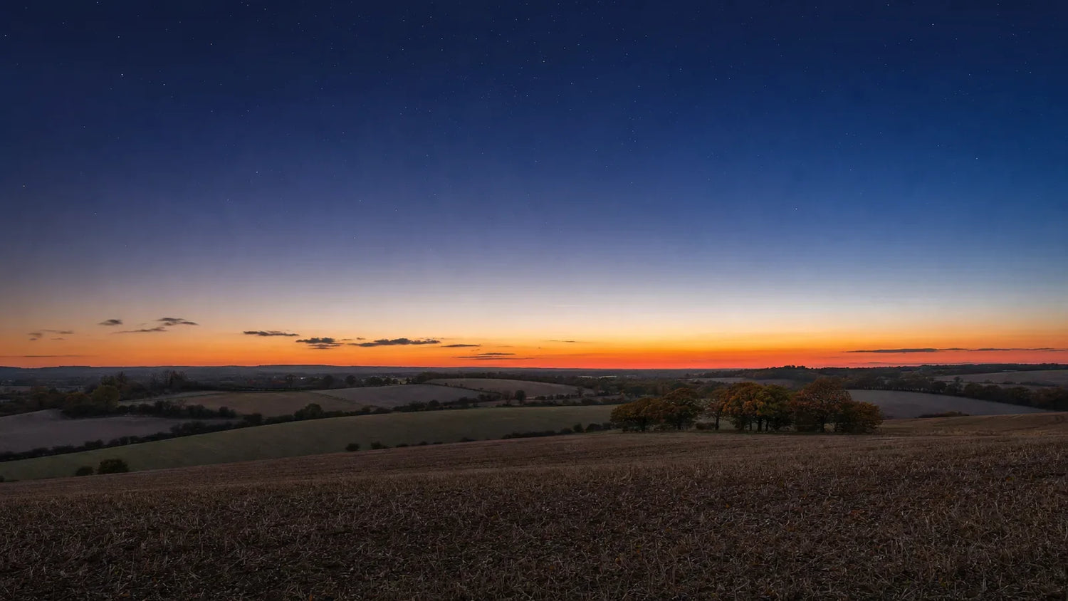 Harvested English fields under an equinox dusk sky, the last band of afterglow along the horizon and the first stars overhead