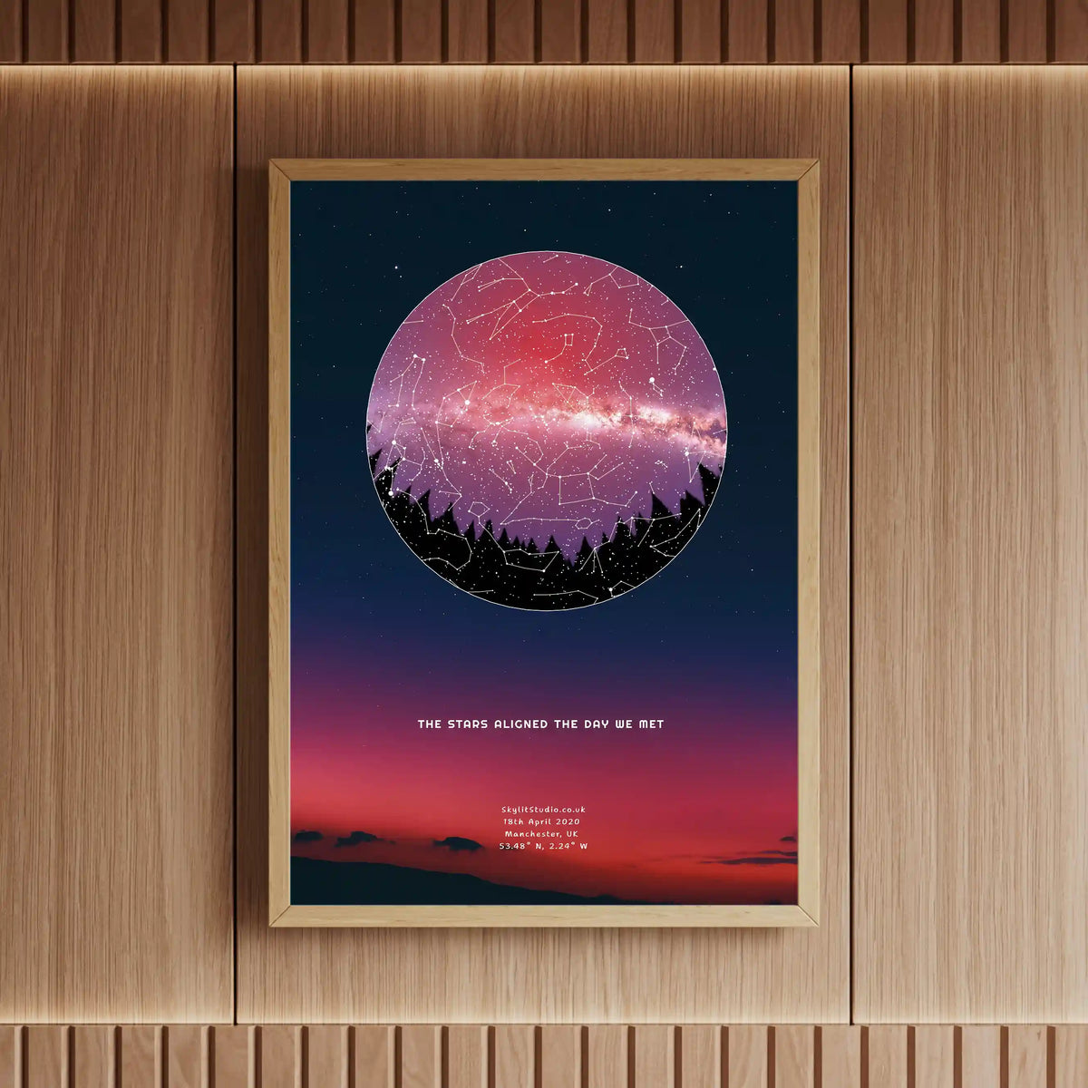 Framed personalised star map print featuring a treeline silhouette and Milky Way sky, displayed on a wooden wall with ambient lighting.