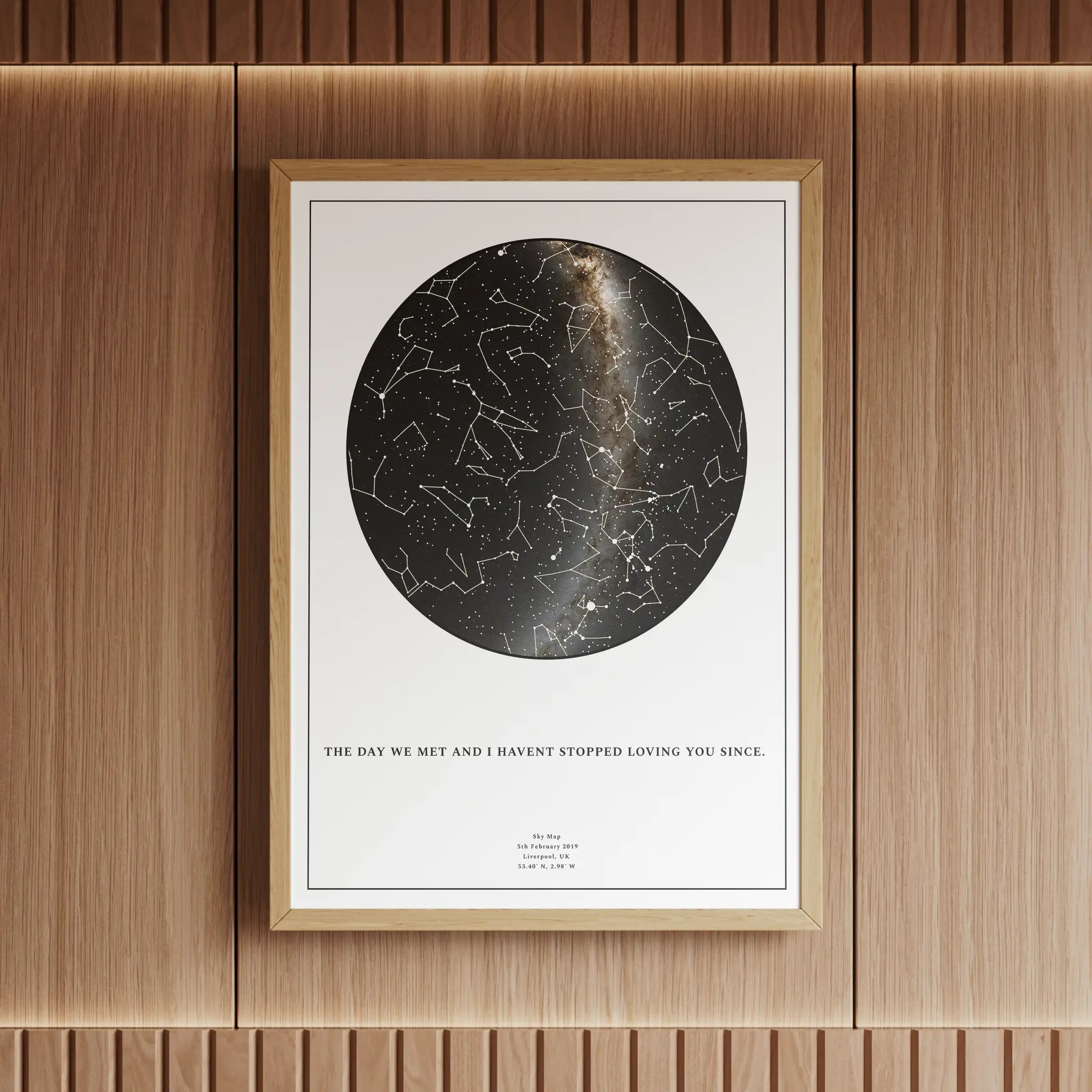 Minimalist personalised star map print with a black and white design, framed in wood and elegantly displayed in a warm, modern interior with ambient lighting. Features constellations and the Milky Way, making it a perfect anniversary or special occasion gift.