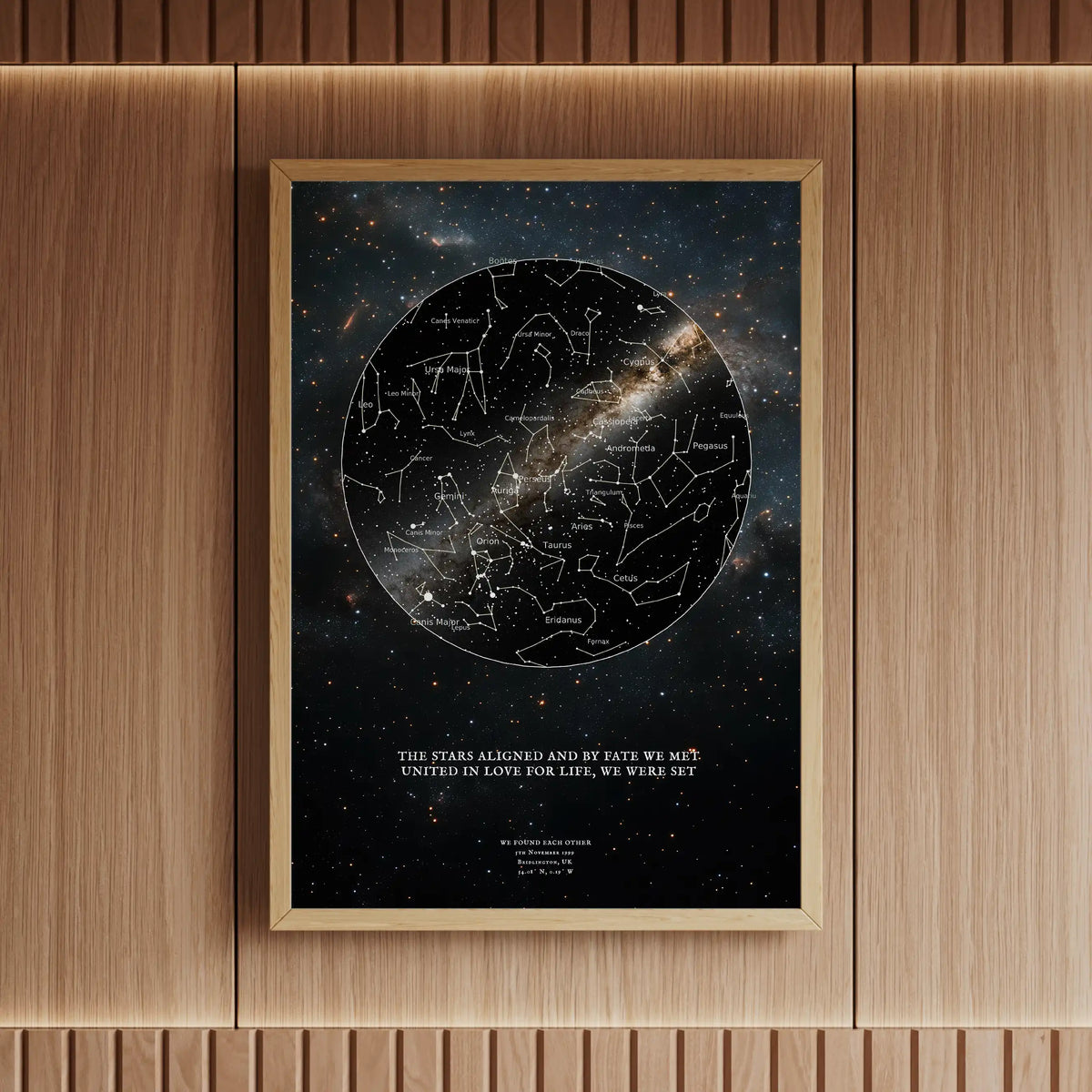 Framed personalised star map print featuring a black constellation design with a galaxy background, elegantly displayed in a wooden interior with warm lighting.