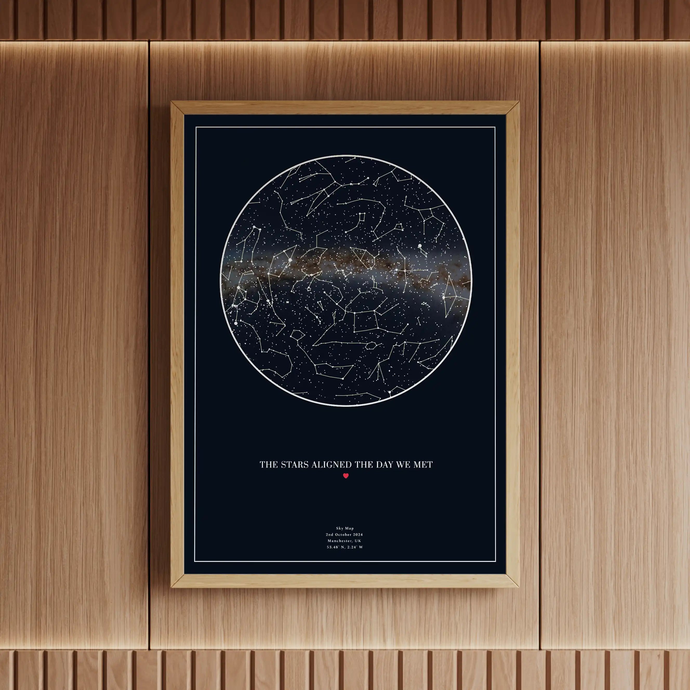 Elegant personalised star map print with a navy blue background and wooden frame, featuring a detailed constellation design and the Milky Way. Displayed in a warm, modern interior with ambient lighting.