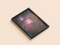 Orion Nebula print in a black frame, flat lay